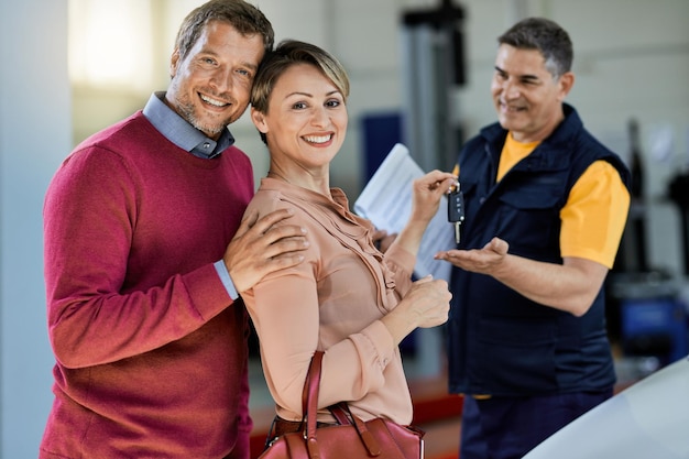 Retrato de clientes felices dando la llave del auto a su mecánico en un taller mientras miran la cámara