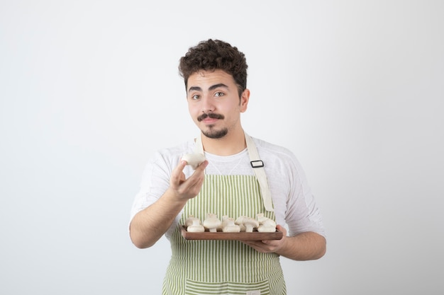 Retrato de cocinero macho mostrando setas crudas en blanco