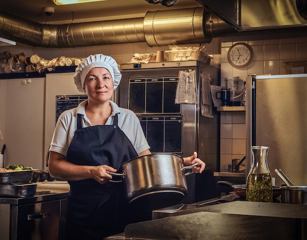 Retrato de un cocinero de mediana edad con uniforme sosteniendo una sartén en la cocina del restaurante.