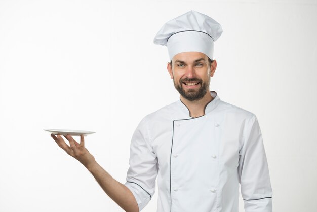 Retrato del cocinero de sexo masculino feliz que sostiene un plato blanco en su mano