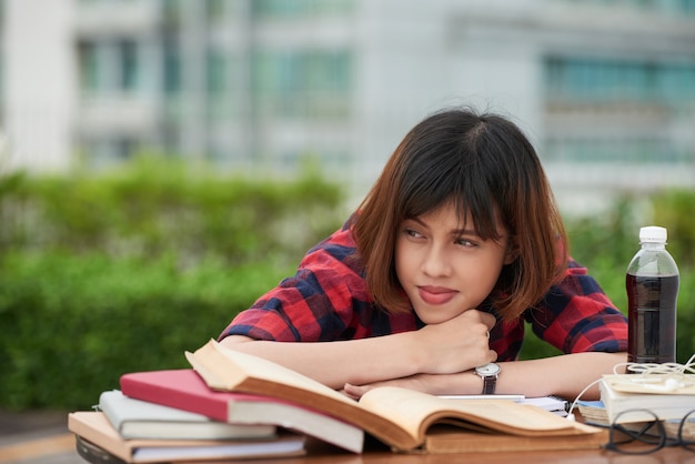 Foto gratuita retrato de colegiala cansada de la rutina de hometask descansando en una mesa llena de libros