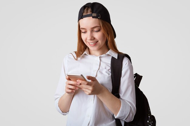 Retrato de colegiala satisfecha juega en línea en un teléfono inteligente durante el descanso en la escuela