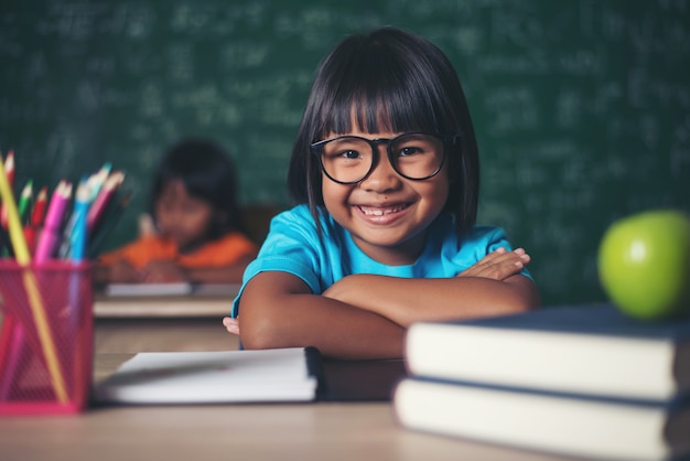 Retrato de colegiala sonriente sentado en la mesa con libros