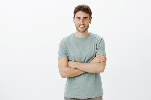 Retrato de un compañero de trabajo masculino alegre y amistoso en traje casual de pie con los brazos cruzados y sonriendo con expresión feliz y amistosa mientras espera que la esposa se vista para caminar