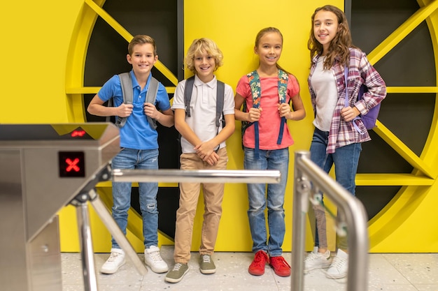 Retrato completo de cuatro lindos niños alegres con ropa informal posando para la cámara en el vestíbulo de un estudio de grabación