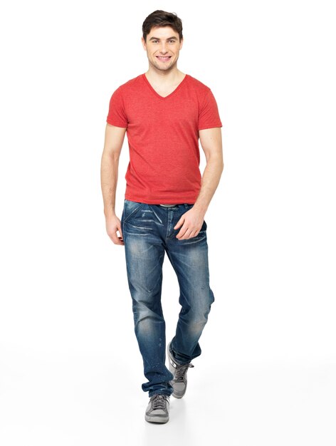 Retrato completo del hombre que camina sonriente en casuals de la camiseta roja aislado en el fondo blanco.