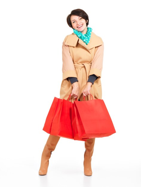 Retrato completo de mujer feliz con bolsas de compras en otoño abrigo con pañuelo verde que se encuentran aisladas en blanco