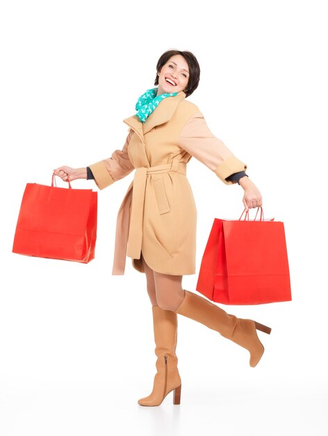 Retrato completo de mujer feliz con bolsas de compras en otoño abrigo con pañuelo verde que se encuentran aisladas en blanco