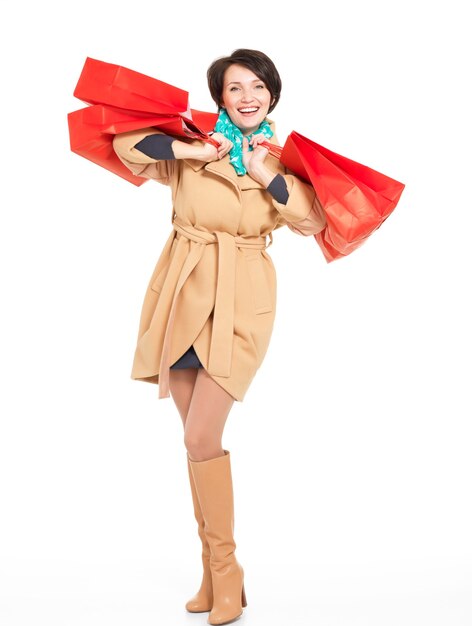 Retrato completo de mujer feliz con bolsas de compras en otoño abrigo con pañuelo verde que se encuentran aisladas en blanco