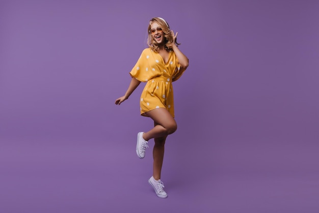 Retrato completo de mujer feliz saltando en traje de verano Foto de estudio de atractiva chica europea expresando felicidad sobre fondo púrpura