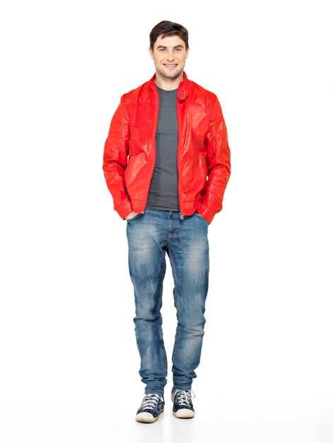 Retrato completo de sonriente feliz guapo en chaqueta roja, jeans y zapatillas deportivas. Hermoso chico de pie aislado en blanco