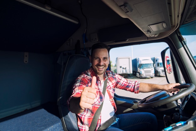 Retrato de conductor de camión motivado profesional sosteniendo Thumbs up en la cabina del camión
