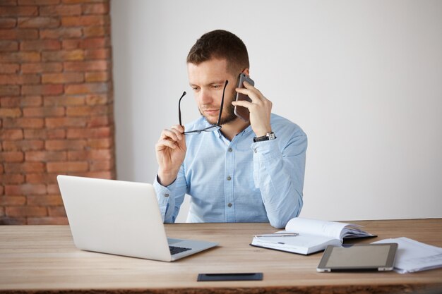 Retrato de contable masculino sin afeitar adulto quitándose gafas, mirando en el monitor del ordenador portátil con expresión cansada