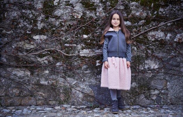 Retrato corporal completo de una adolescente con falda rosa y chaqueta gris sobre fondo de roca congelada.