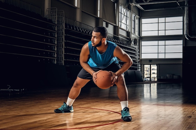 Retrato corporal completo del jugador de baloncesto profesional negro en una acción en el campo de baloncesto.