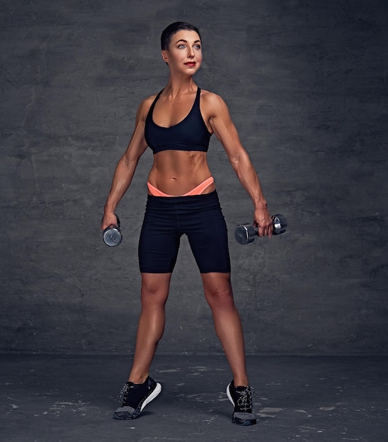 Retrato corporal completo de una mujer deportiva de pelo corto de mediana edad sostiene pesas.