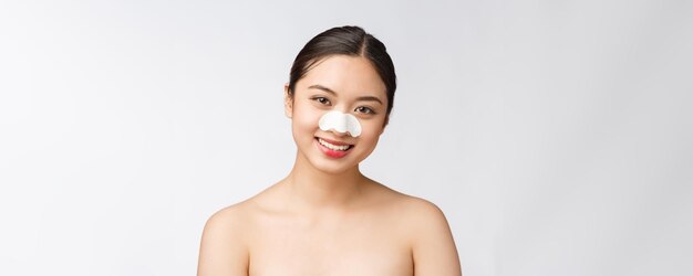 Retrato de cosmetología de hermosa modelo asiática femenina con máscara en la nariz Primer plano de mujer joven sana con piel suave pura y maquillaje natural fresco