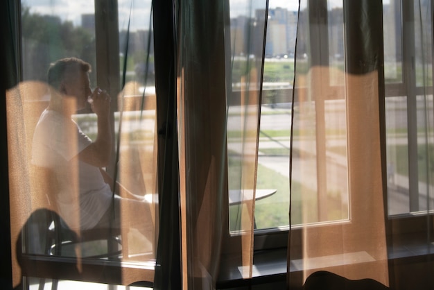 Retrato creativo del hombre con cortinas y sombras desde la ventana.