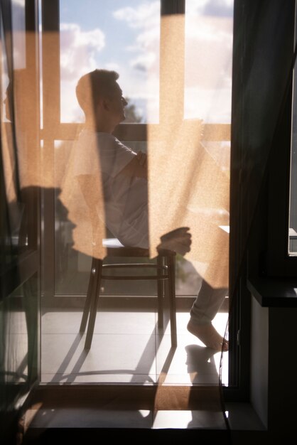 Retrato creativo del hombre con cortinas y sombras desde la ventana.