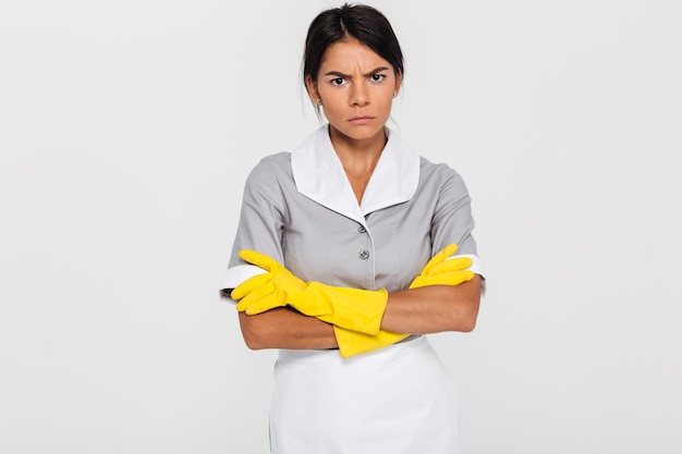 Foto gratuita retrato de criada atractiva gruñón en uniforme y guantes de goma amarilla de pie con las manos cruzadas