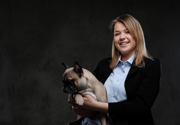 Retrato de una criadora rubia sonriente sostiene su lindo pug. Aislado en un fondo de textura oscura.