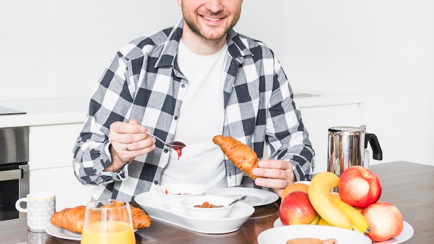 Retrato de un croissant joven feliz comiendo en el desayuno