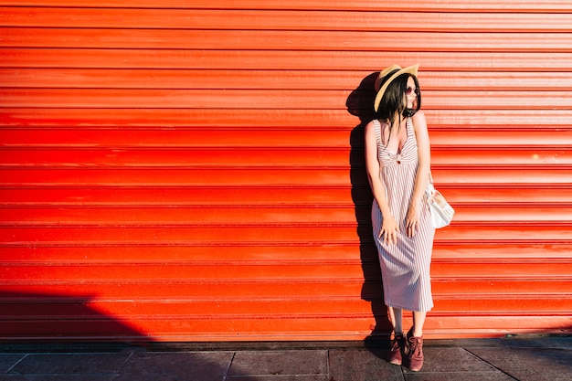 Retrato de cuerpo entero de una adorable niña con sombrero de moda y vestido largo de pie al aire libre