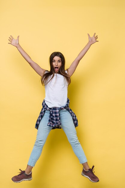 Retrato de cuerpo entero de una alegre mujer caucásica casual saltando aislada sobre fondo amarillo