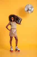 Foto gratuita retrato de cuerpo entero de alegre mujer disco africana con la mano en su cintura vistiendo ropas retro de pie sobre patines, sosteniendo boombox