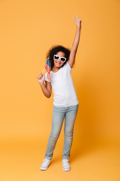 Retrato de cuerpo entero de una alegre niña africana con bandera americana