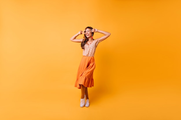 Retrato de cuerpo entero de una chica emocional de moda bailando en brillante. Señora jocund en falda larga naranja que expresa felicidad.