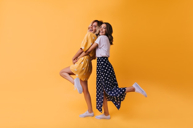 Retrato de cuerpo entero de una chica fascinante en falda larga bailando con un amigo. Alegres modelos femeninos con ropa elegante que expresan felicidad.