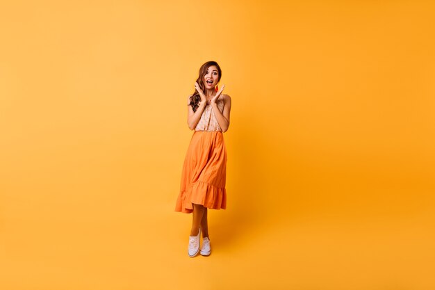 Retrato de cuerpo entero de una chica increíble en traje de verano brillante. Mujer morena alegre posando en amarillo con sonrisa de sorpresa.