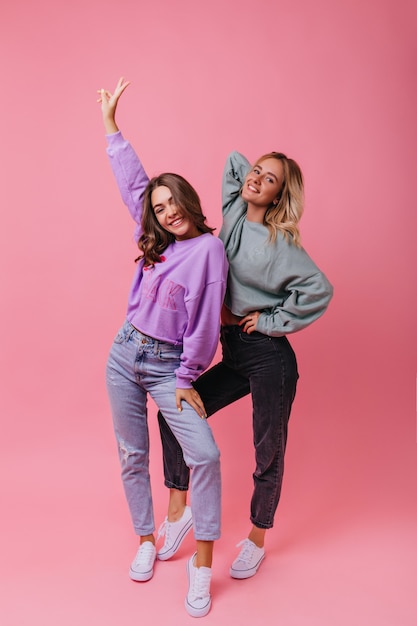 Retrato de cuerpo entero de chicas maravillosas en traje de calle vintage. Señoras de moda caucásicas bailando en rosa.