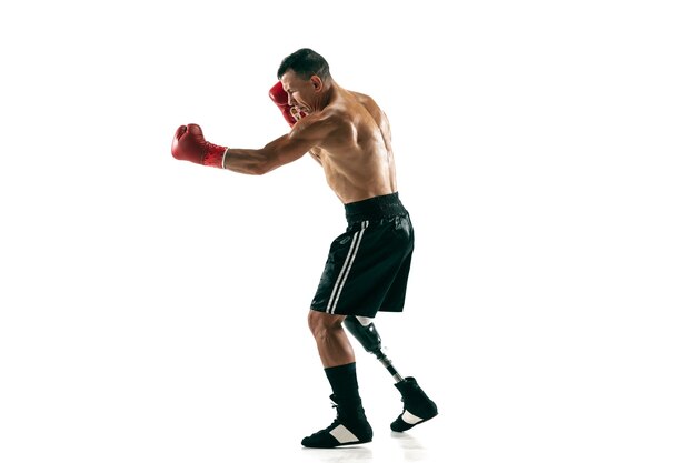 Retrato de cuerpo entero de deportista musculoso con prótesis de pierna, espacio de copia. Boxeador masculino en guantes rojos. Disparo aislado en la pared blanca.