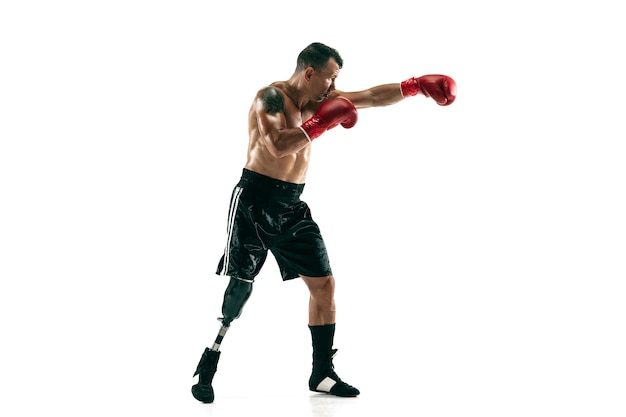 Retrato de cuerpo entero de deportista musculoso con prótesis de pierna, espacio de copia. Boxeador masculino en guantes rojos. Disparo aislado en la pared blanca.