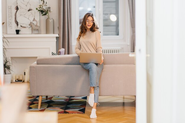 Retrato de cuerpo entero de hermosa mujer independiente en jeans haciendo su trabajo, usando laptop