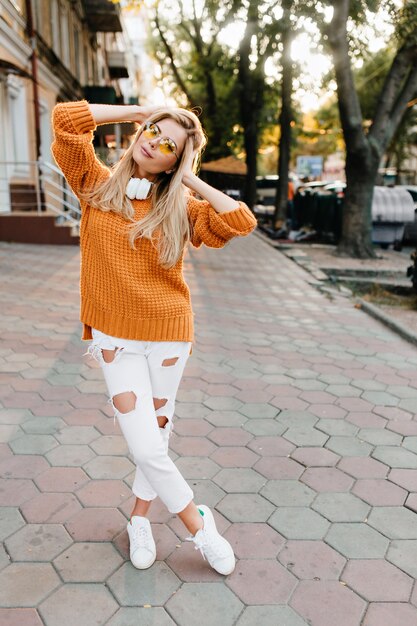 Retrato de cuerpo entero de hermosa mujer con zapatos blancos y pantalones rotos jugando con cabello rubio