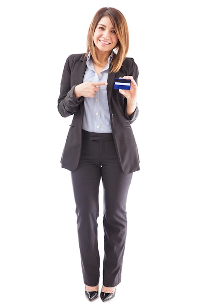 Retrato de cuerpo entero de una hermosa representante bancaria femenina apuntando a una tarjeta de crédito y sonriendo