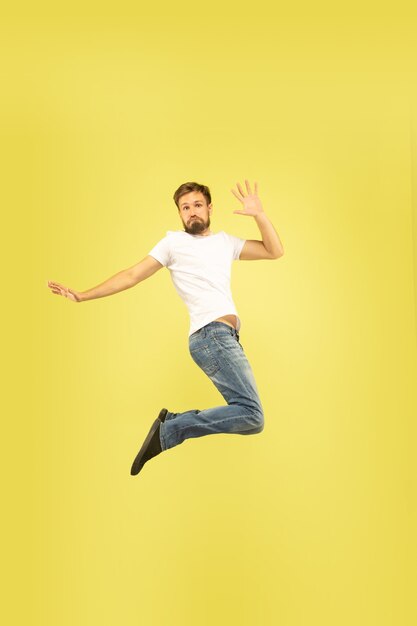 Retrato de cuerpo entero de hombre feliz saltando aislado sobre fondo amarillo. Modelo masculino caucásico en ropa casual. Libertad de elección, inspiración, concepto de emociones humanas. Da cinco, saluda, confiado.