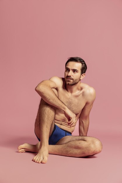 Retrato de cuerpo entero de un hombre guapo posando shitrless en ropa interior azul aislado en la pared rosa