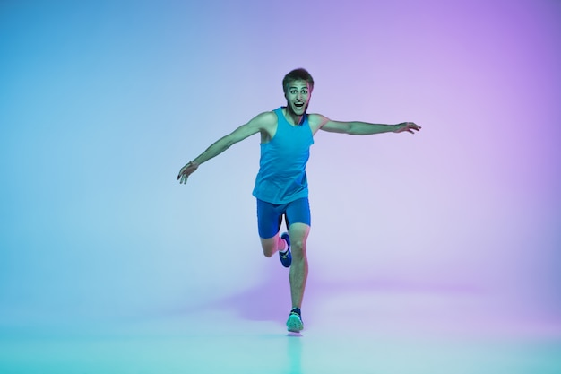 Retrato de cuerpo entero de un hombre joven activo corriendo, caucásico, corriendo en estudio de gradiente en luz de neón