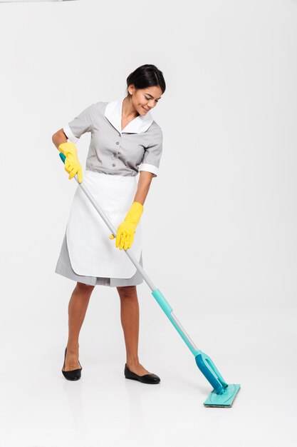 Retrato de cuerpo entero de joven atractiva en uniforme de limpieza de piso con un trapeador