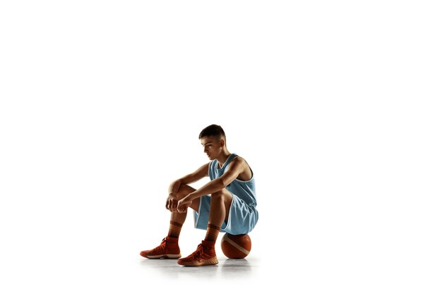 Retrato de cuerpo entero del joven jugador de baloncesto con una pelota aislada sobre fondo blanco de estudio. Adolescente seguro posando con pelota. Concepto de deporte, movimiento, estilo de vida saludable, anuncio, acción, movimiento.