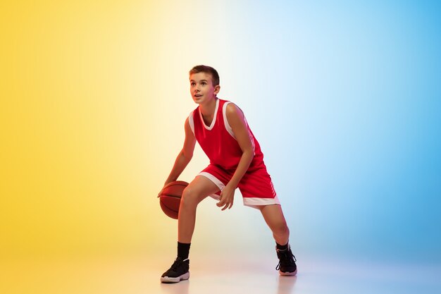 Retrato de cuerpo entero de un joven jugador de baloncesto con pelota sobre fondo degradado