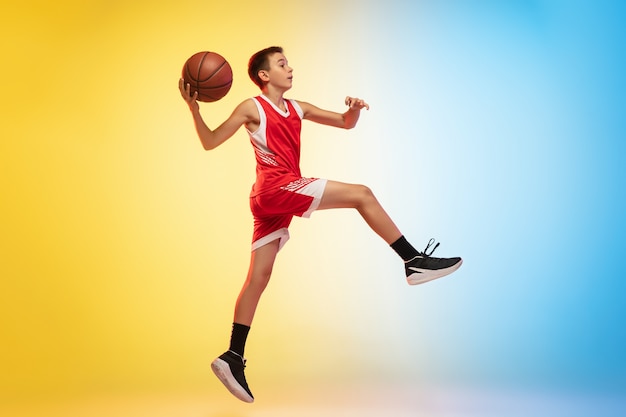 Retrato de cuerpo entero de un joven jugador de baloncesto con pelota sobre fondo degradado