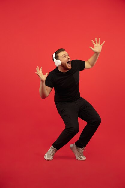 Retrato de cuerpo entero de un joven salto alto aislado en la pared roja. Modelo masculino caucásico. Copyspace. Las emociones humanas, la expresión facial, el concepto de deporte.