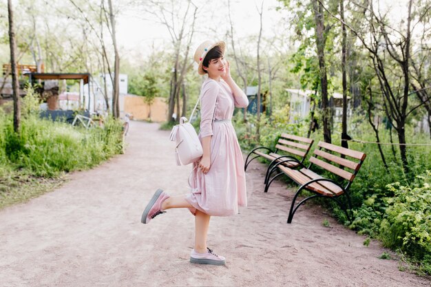 Retrato de cuerpo entero de una linda dama morena, posando en medio del callejón del parque en la mañana