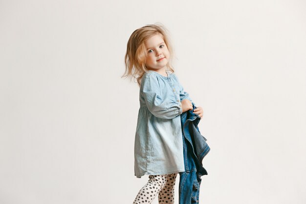 Retrato de cuerpo entero de una linda niña pequeña en ropa de jeans con estilo y sonriente, de pie en blanco. Concepto de moda infantil