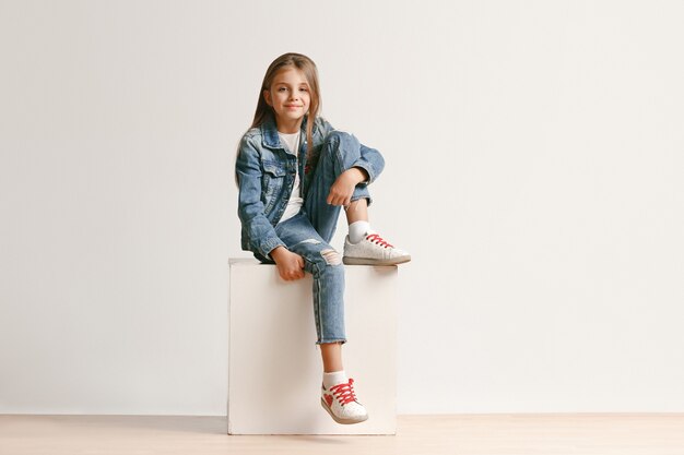 Retrato de cuerpo entero de lindo adolescente en ropa de jeans con estilo mirando a cámara y sonriendo